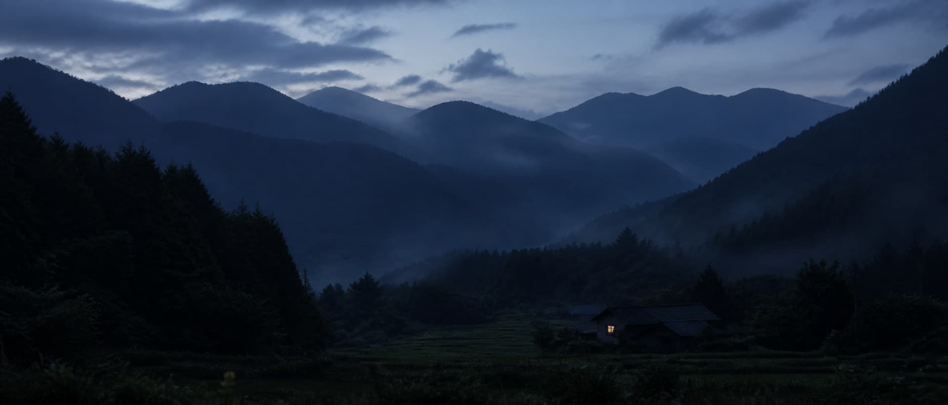 夕暮れの山々と谷あいに灯る小さな家